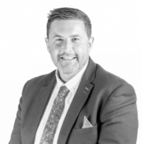 grey filtered headshot of Tom Fishwick in suit and tie